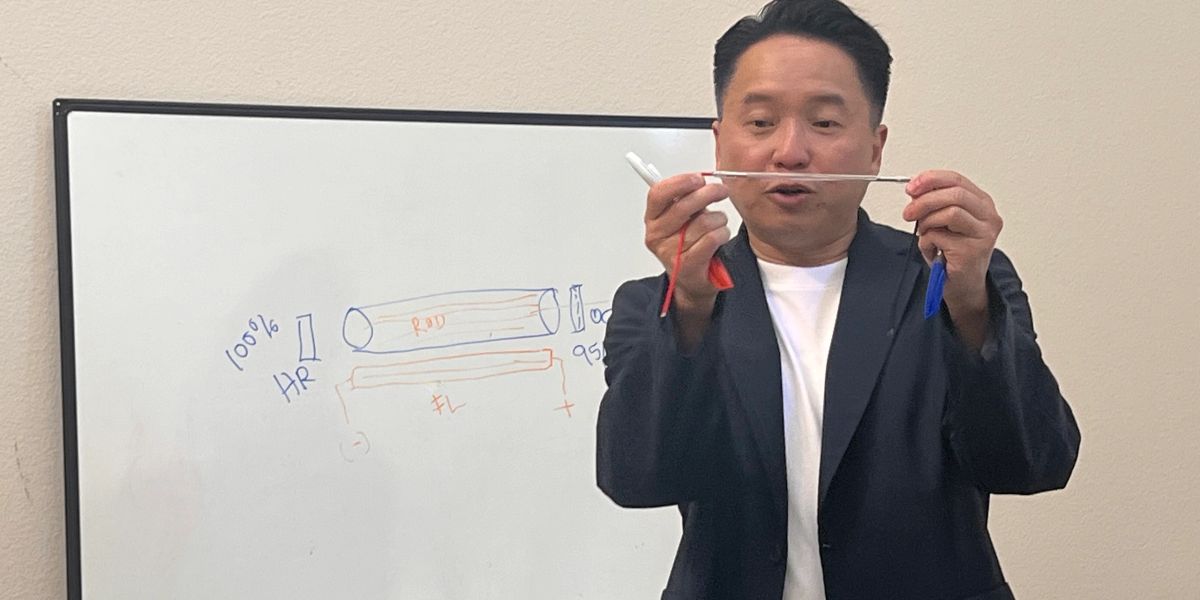 Amaury teaching laser physics at a whiteboard, holding a laser rod